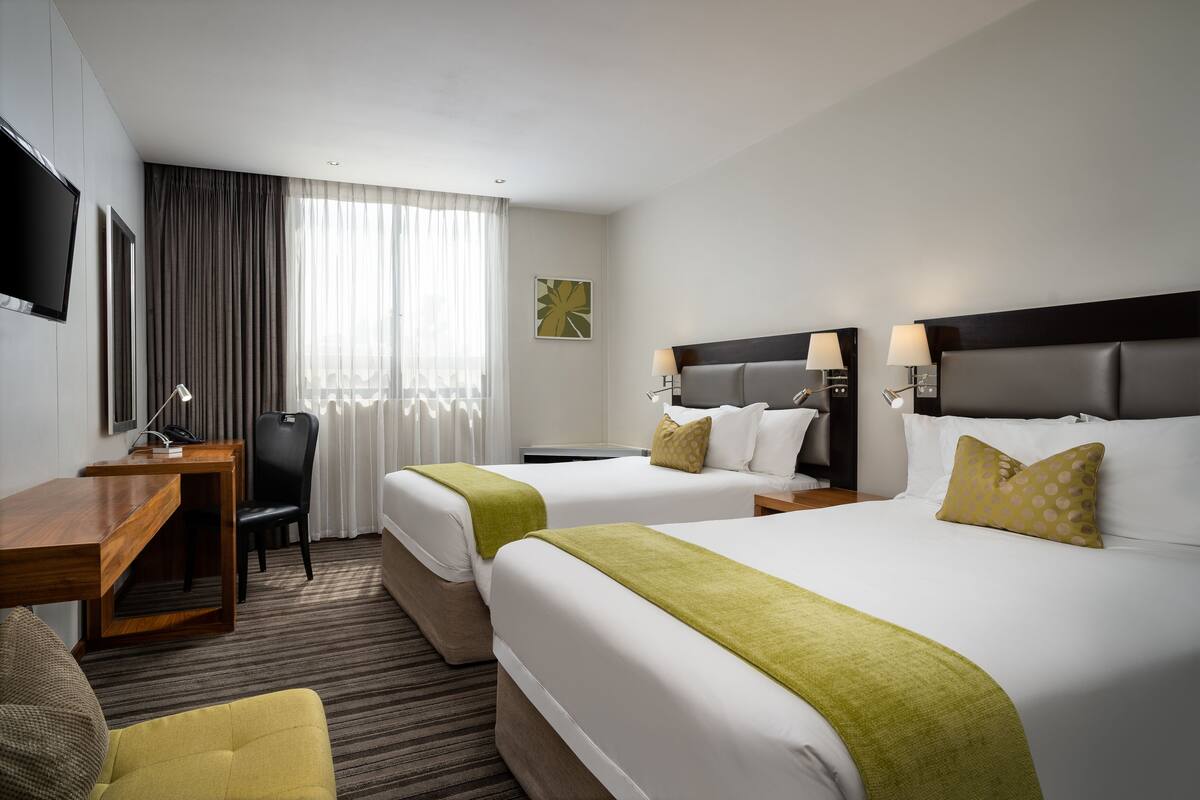 A hotel room with two beds, a desk, a chair, a TV, and a window with curtains.