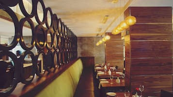 A restaurant interior with a long bench seating area, wooden walls, and circular mirrors on the left.