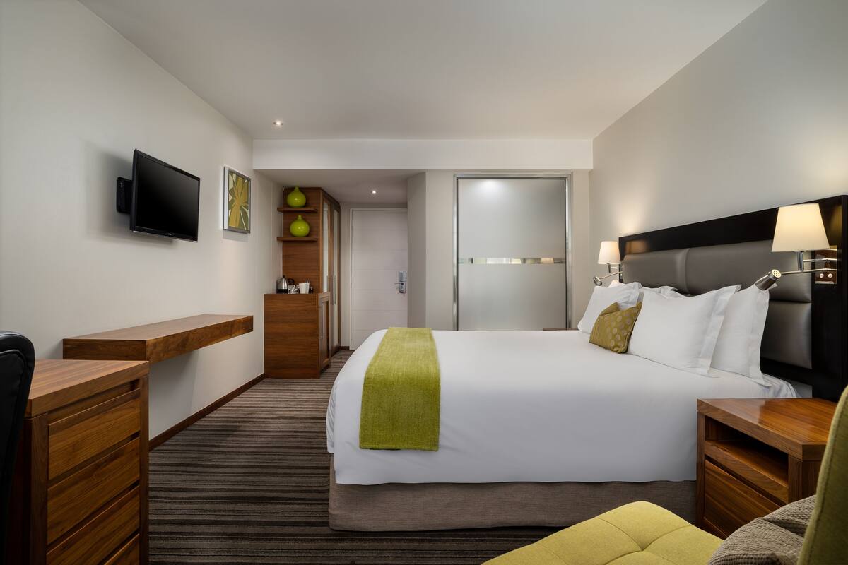A hotel room with a bed, a desk, a TV, a wardrobe, and a bathroom.