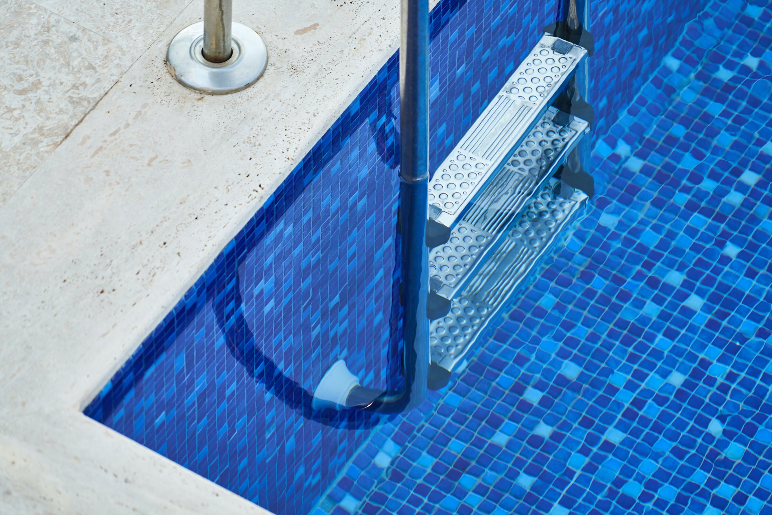 Una porzione di piscina con piastrelle di mosaico blu e una scala in metallo.