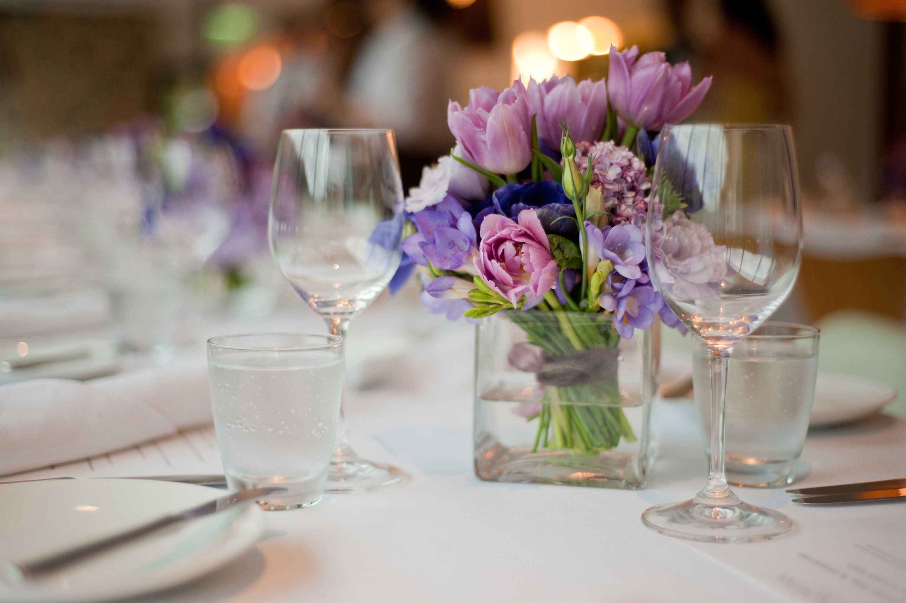 A table set with wine glasses and a vase of flowers.
