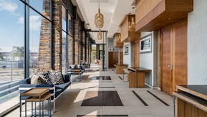 A modern hotel lobby with a seating area, wooden accents, and large windows offering a view of palm trees. - Premier Hotel Midrand (Midrand)