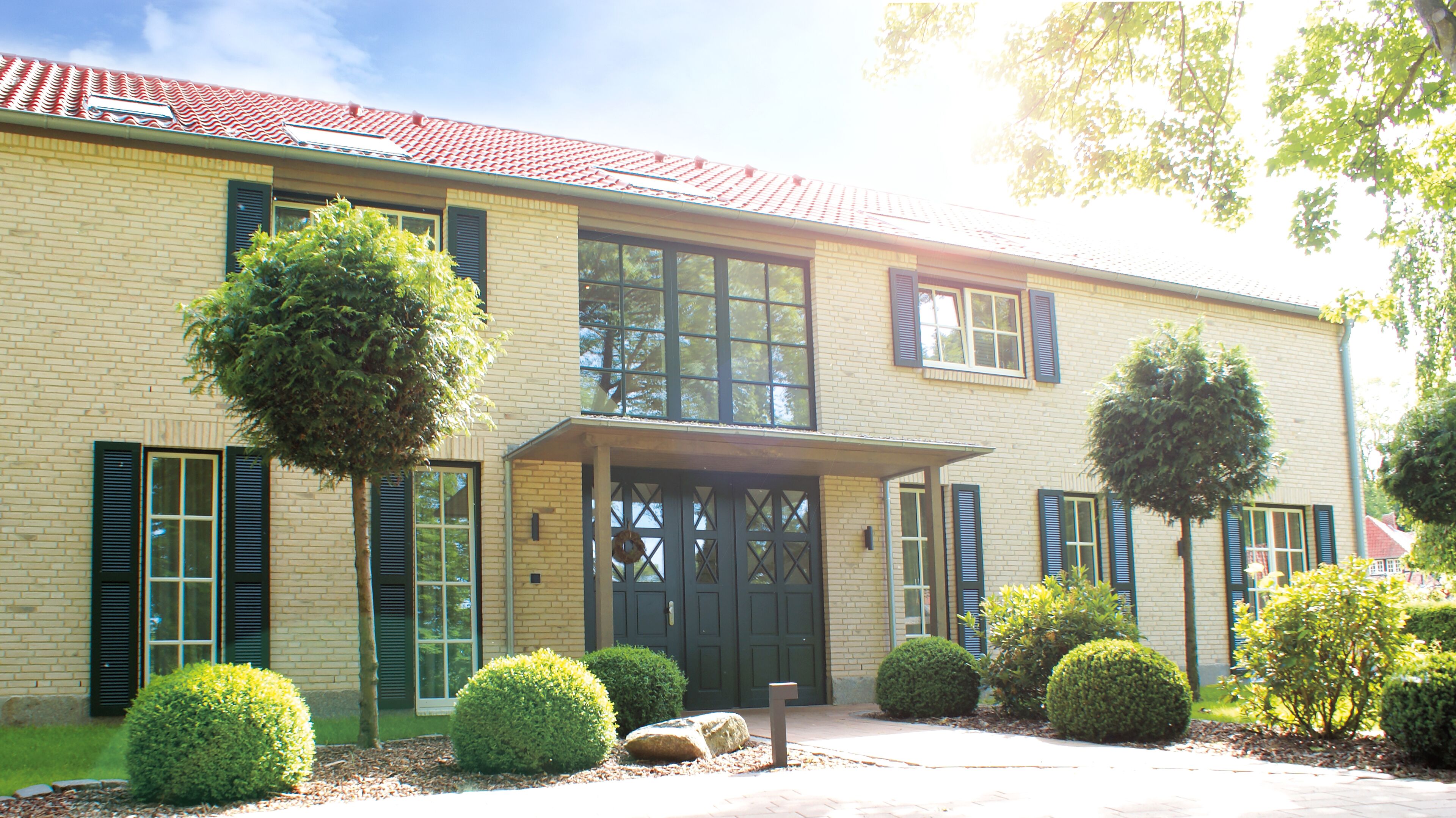 A two-story building with a brick facade, green shutters, and a red-tiled roof.