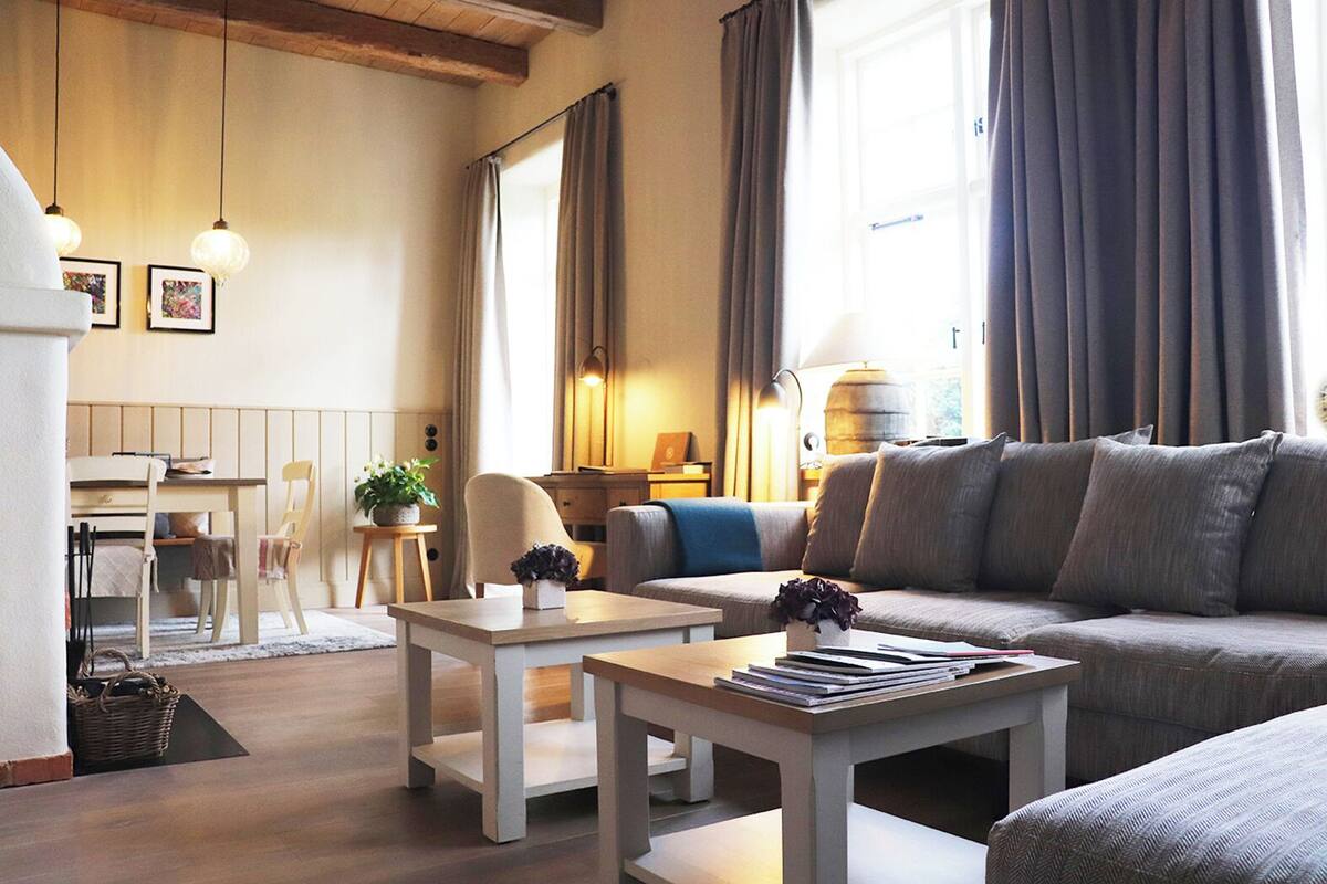 Un salon bien éclairé, avec un canapé, une table basse, un coin repas avec des chaises et une lampe.