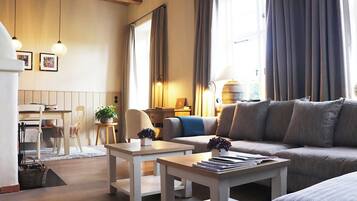 Ett väl upplyst vardagsrum med en soffa, ett soffbord, en matplats med stolar och en lampa.