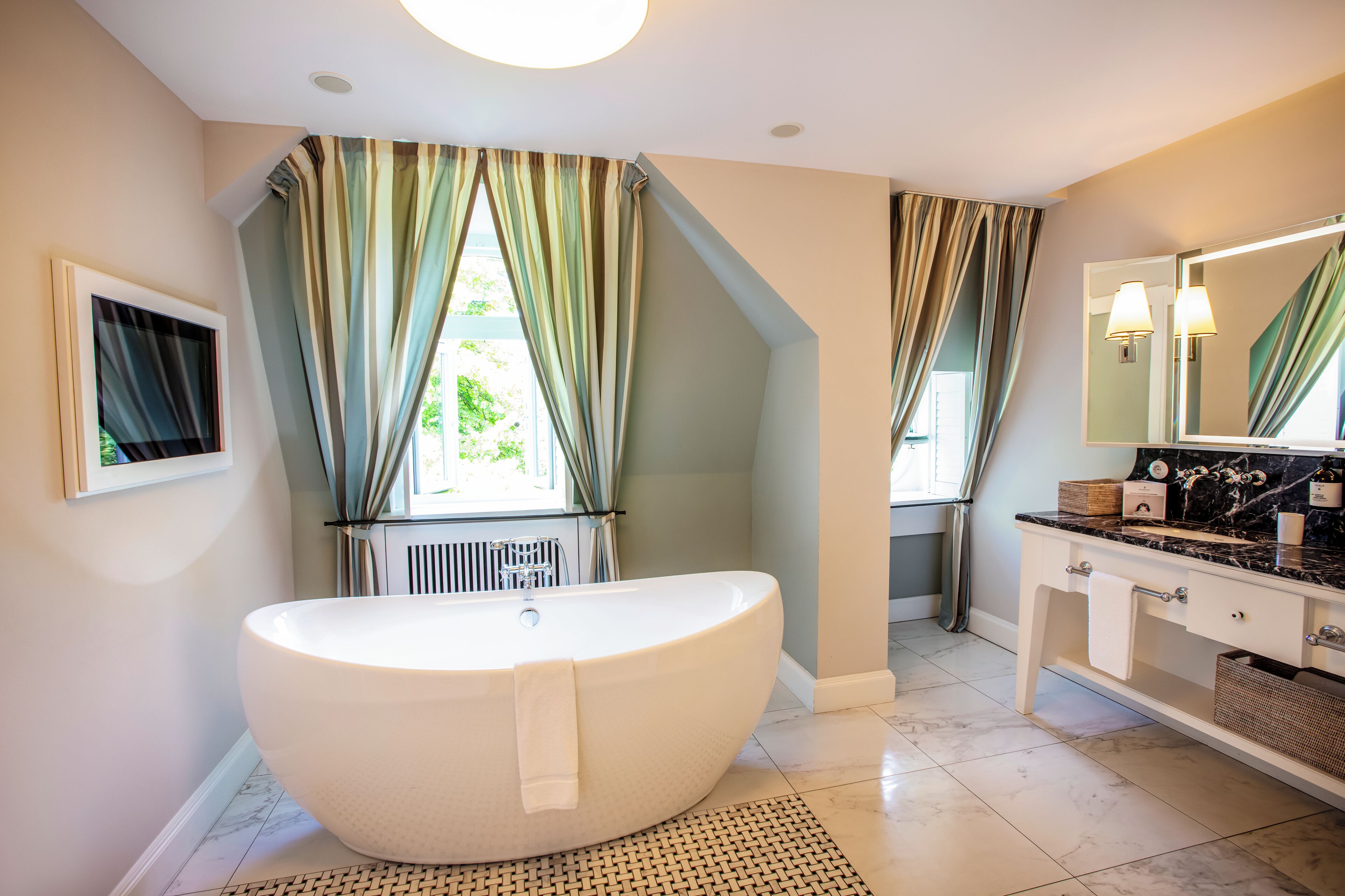 Un bagno moderno con una vasca da bagno freestanding, un mobile toilette con specchio e una finestra con tende.
