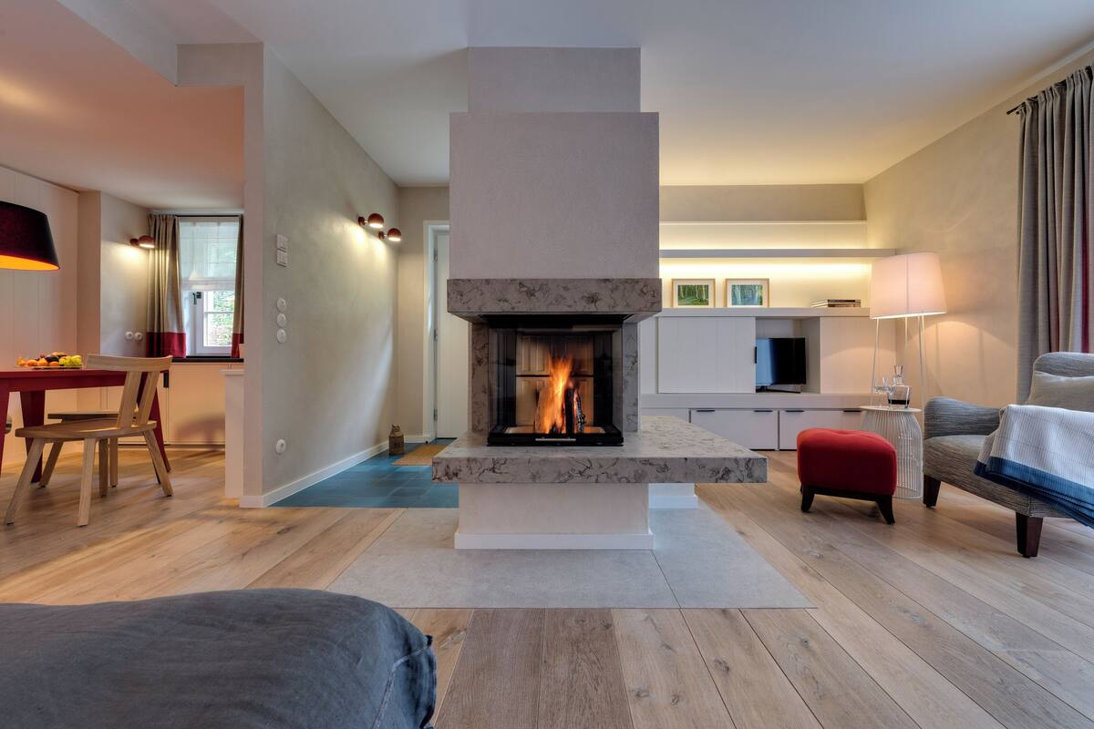 Un salon moderne doté d’une cheminée, de parquet, d’un coin repas et d’un espace détente avec un canapé et un pouf.