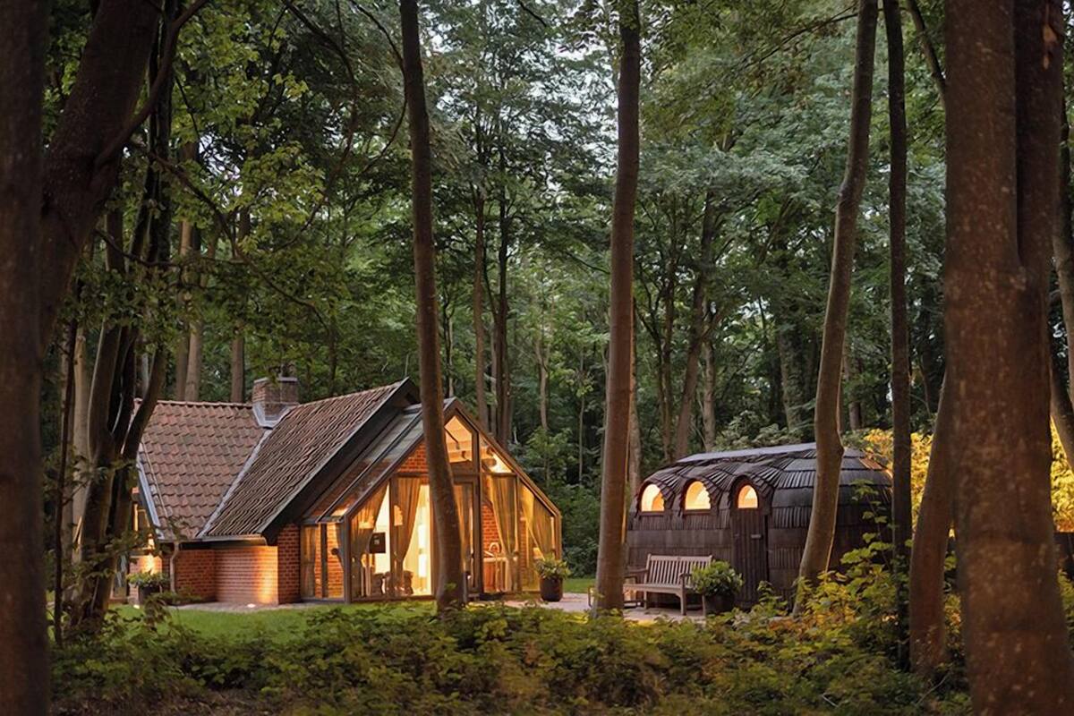 Un chalet rustique, doté d’un toit en pente et de grandes fenêtres, entouré d’une forêt dense.