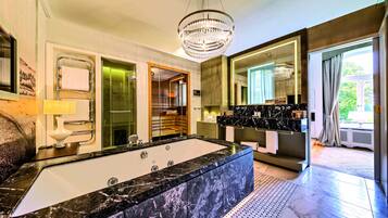 A modern bathroom with a large marble bathtub, a chandelier, and a large mirror.
