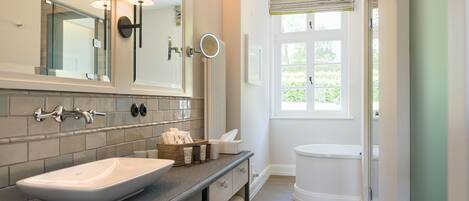 A modern bathroom with a large mirror, a vessel sink, a toilet, and a window with a view of greenery.