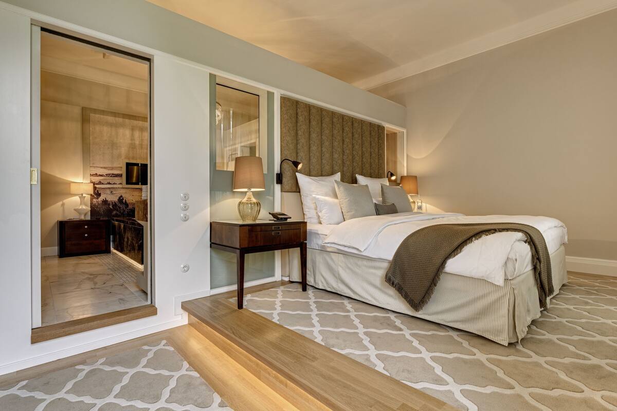 Une chambre à coucher comprenant un lit, des tables de chevet, une commode, un miroir et une porte coulissante donnant sur une autre pièce.