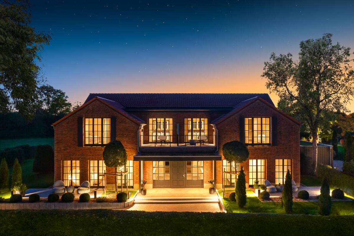 Une maison à deux étages, construite en briques, dotée de grandes fenêtres, d’un balcon et d’une allée bien éclairée.