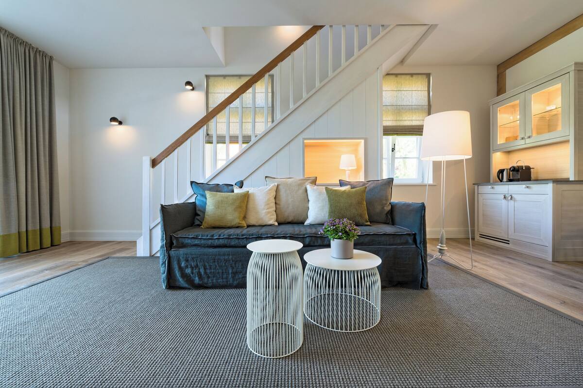 Un salon moderne avec un escalier, un ensemble de canapés, deux petites tables rondes et une lampe.