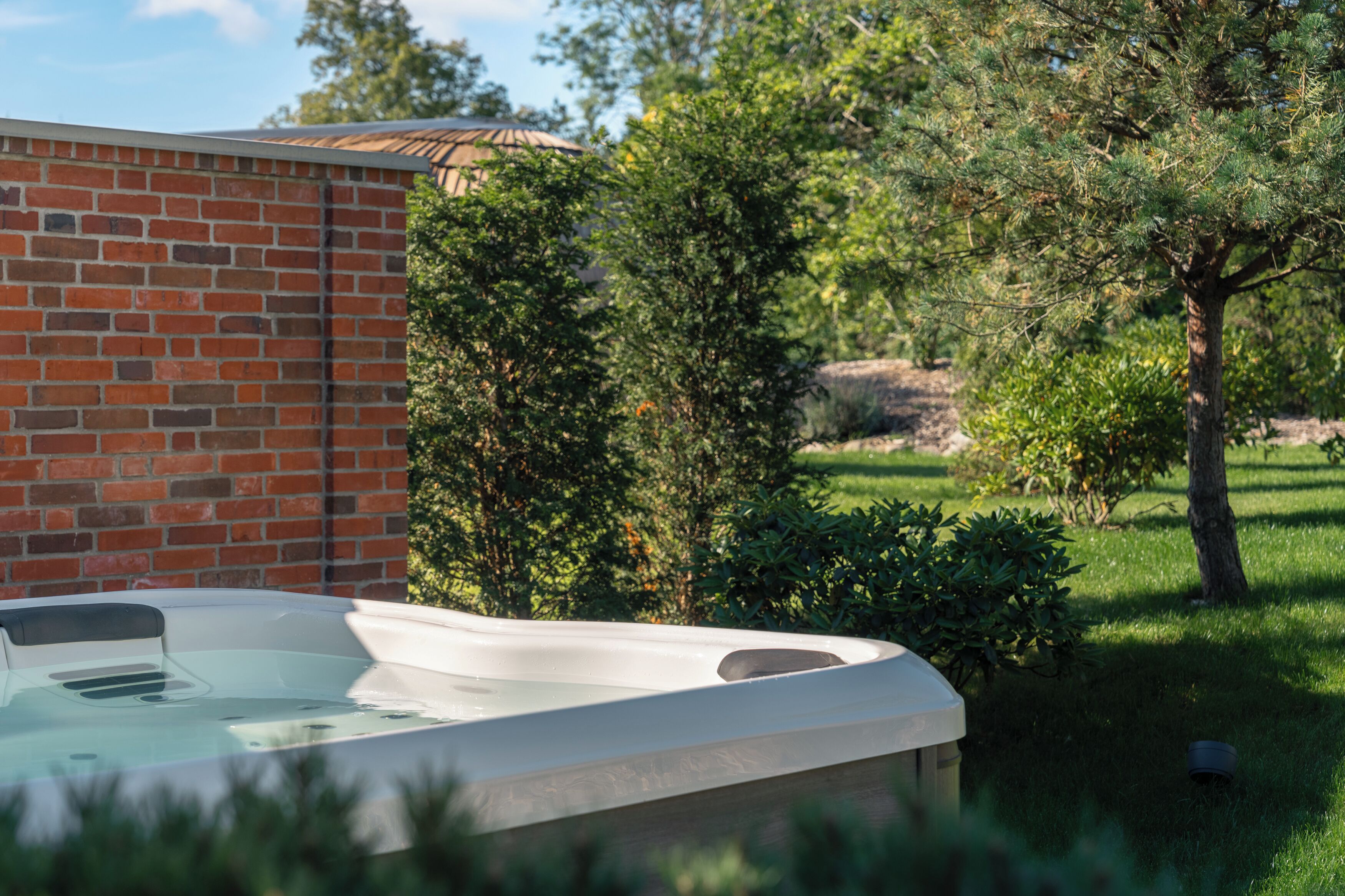 A hot tub in a garden with a brick wall and trees.