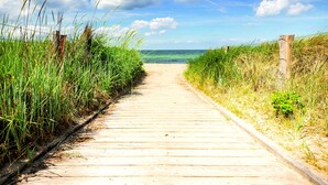 Een houten looppad naar het strand, met gras aan beide zijden.