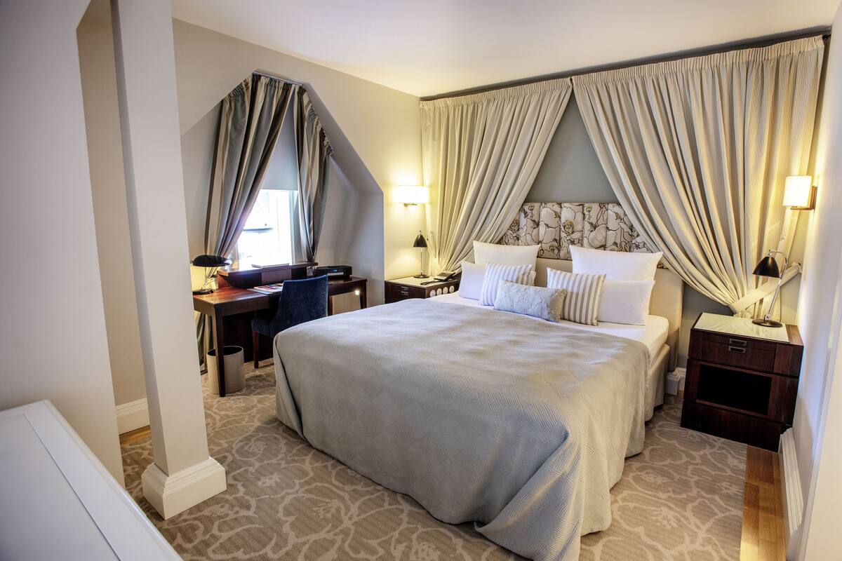 Une chambre d’hôtel avec un grand lit, un bureau, une chaise et deux tables de chevet équipées de lampes.