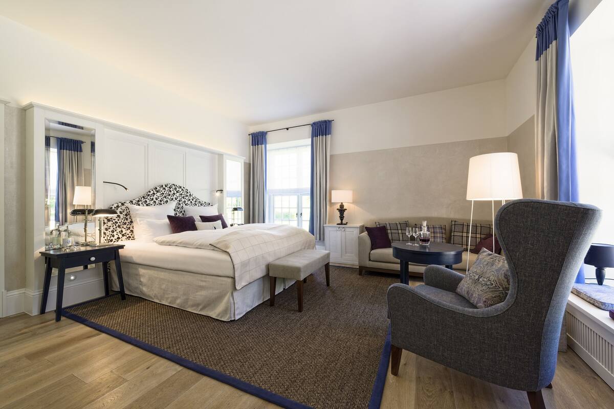 Une chambre d’hôtel avec un grand lit, une chaise, une petite table et une fenêtre avec des rideaux.