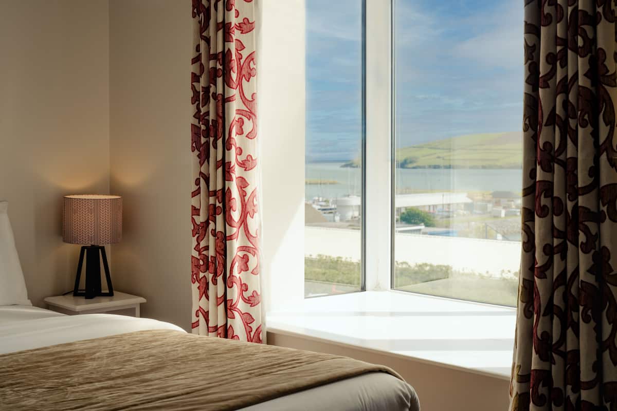 A hotel room with a large window, a bed, a bedside lamp, and curtains.