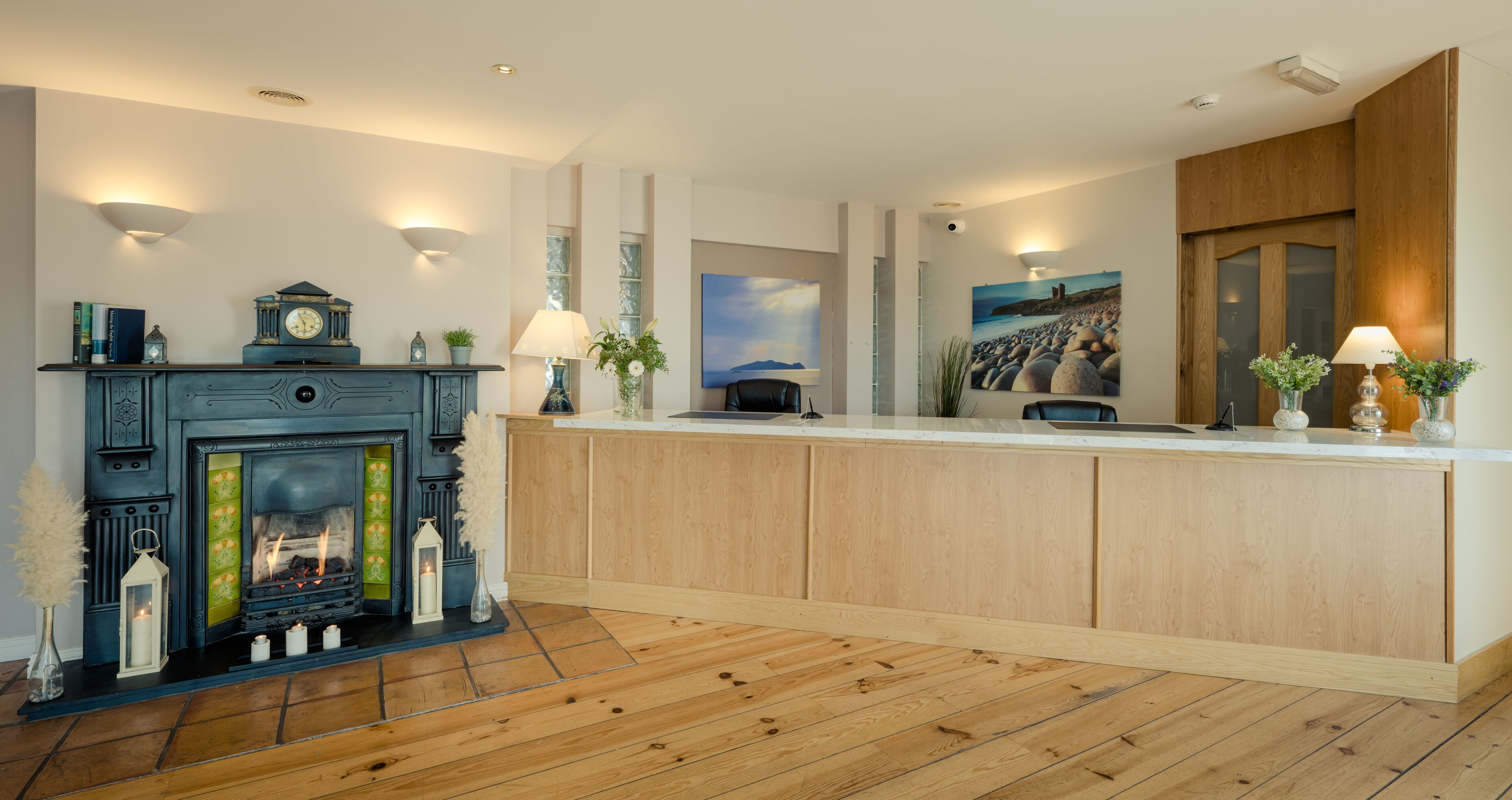 A modern hotel lobby with a fireplace, wooden flooring, a reception desk, and wall-mounted lighting.