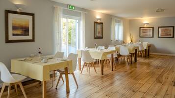 A dining area with multiple tables and chairs, wooden flooring, and framed artwork on the walls.