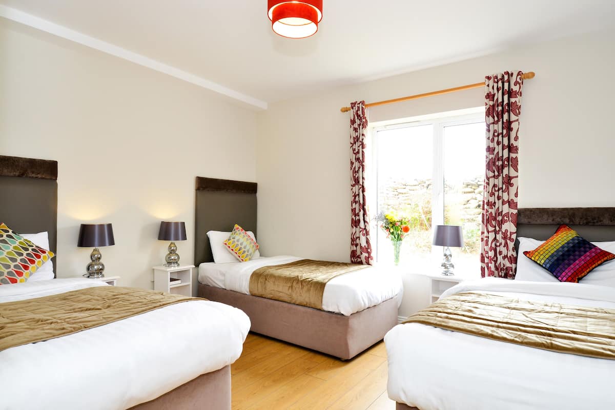 A hotel room with two beds, a window with curtains, bedside lamps, and a wooden floor.