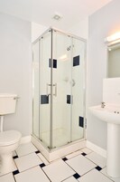 Un baño con ducha de mampara de vidrio, inodoro blanco y lavamanos con espejo.