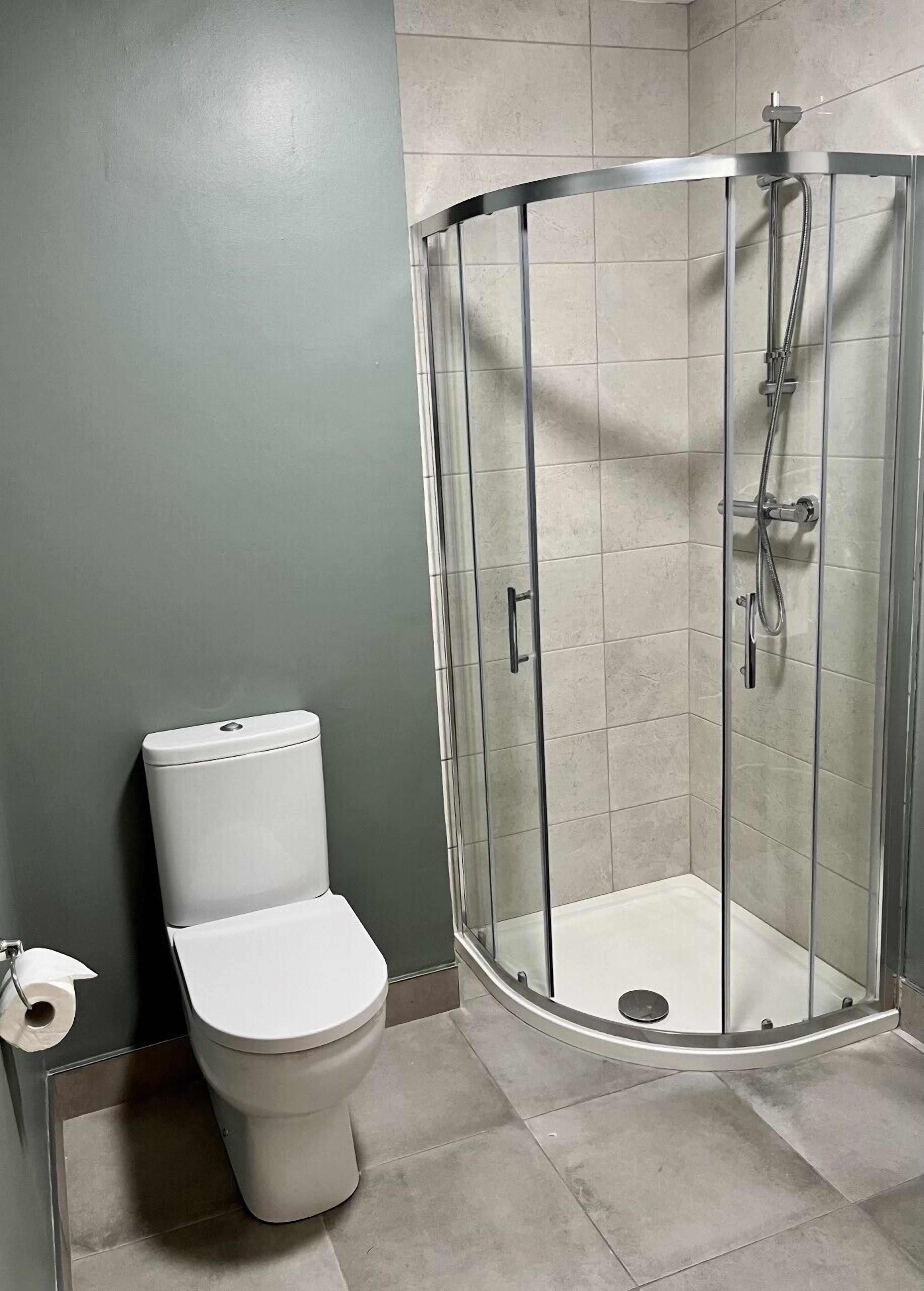Et moderne badeværelse med en brusekabine i glas, toilet og et håndklædestativ.