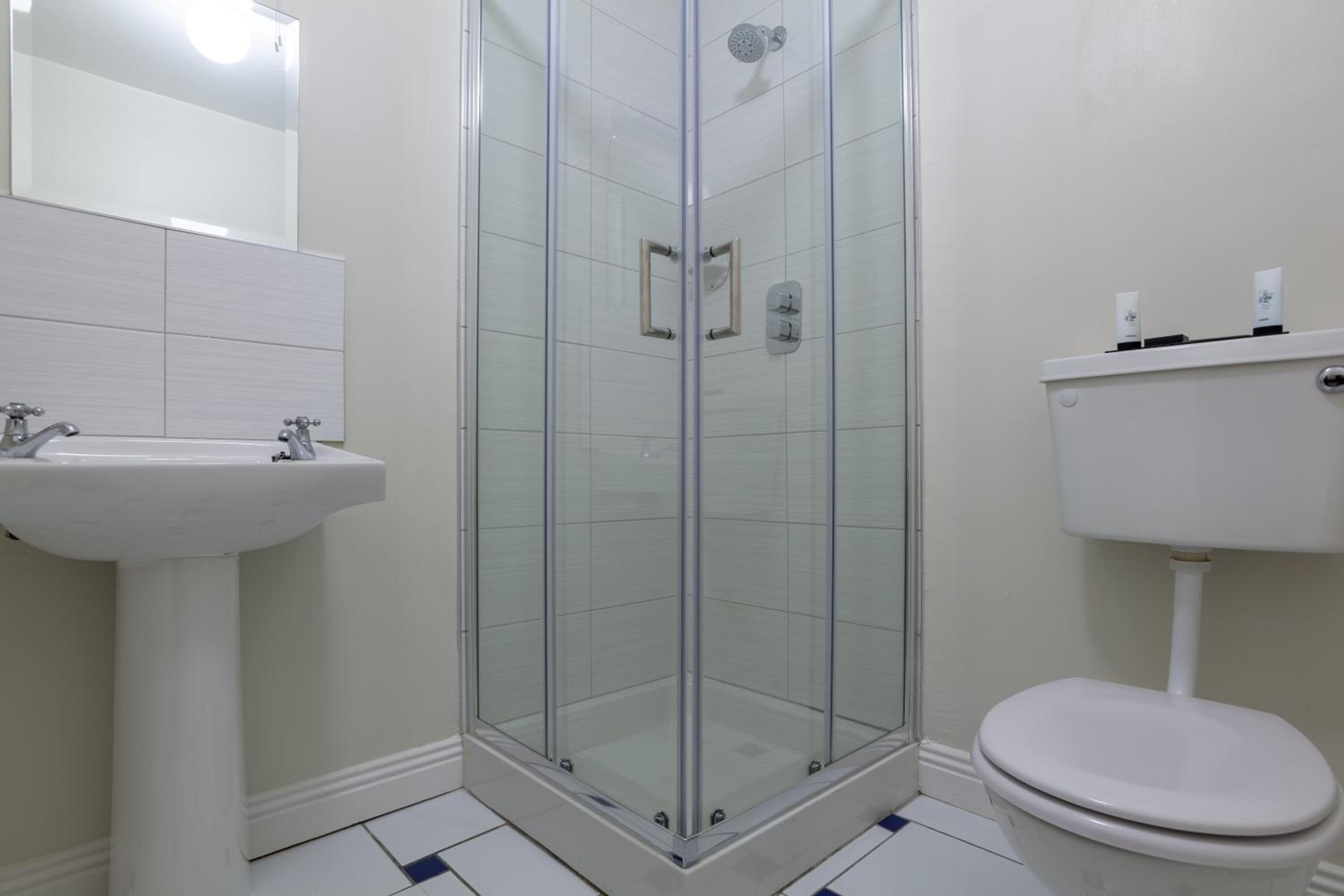 Een badkamer met een douchecabine van glas, een witte wastafel en een toilet.