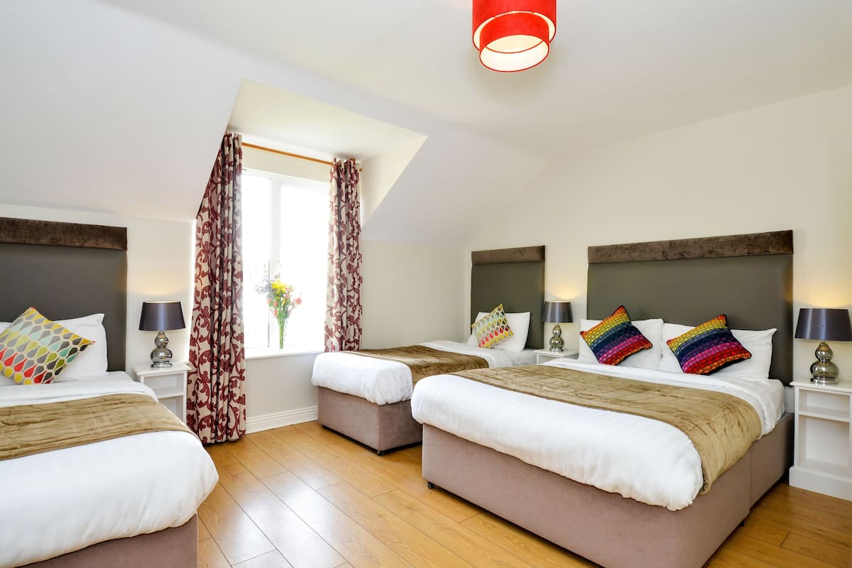 A hotel room with two beds, a window with curtains, a red light fixture, and a wooden floor.