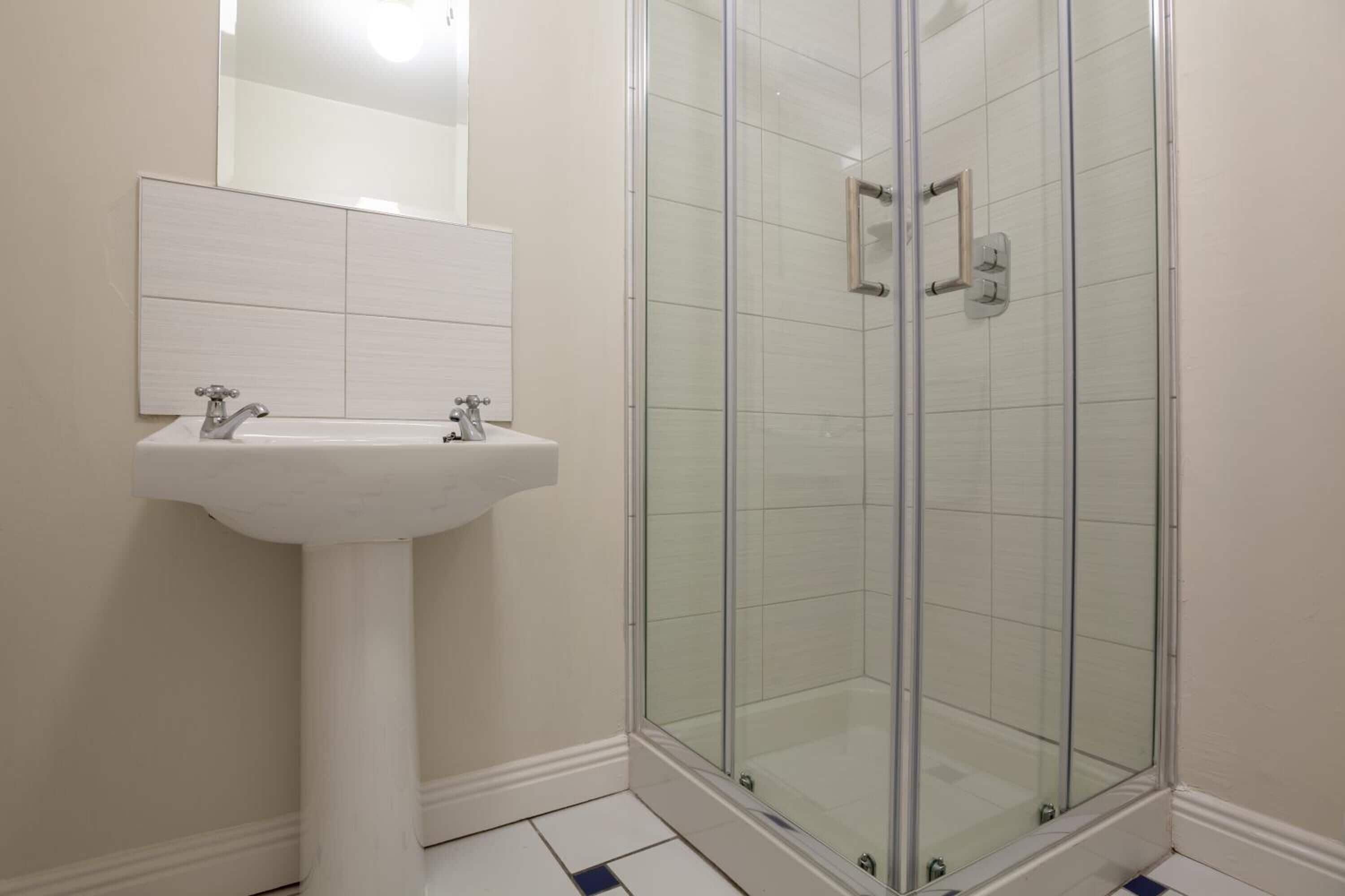 Un baño con lavamanos blanco, un espejo y cabina de ducha con puertas de vidrio.