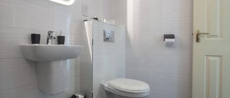 Une salle de bain moderne avec un lavabo blanc, des toilettes et un miroir doté d’un éclairage intégré.