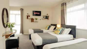 A hotel room with two beds, a TV mounted on the wall, a desk with a chair, and a window with curtains.
