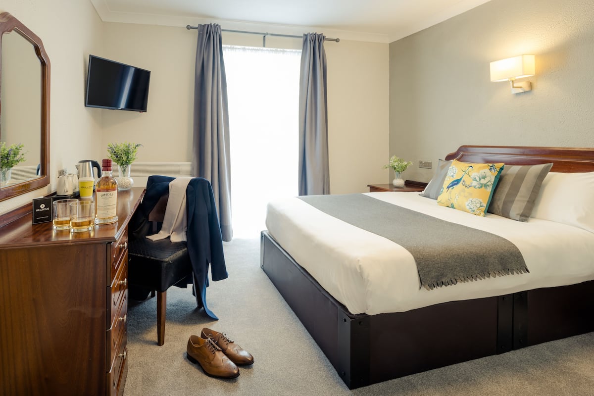 Habitación de hotel con cama, escritorio con silla, televisor montado en la pared y ventana con cortinas.