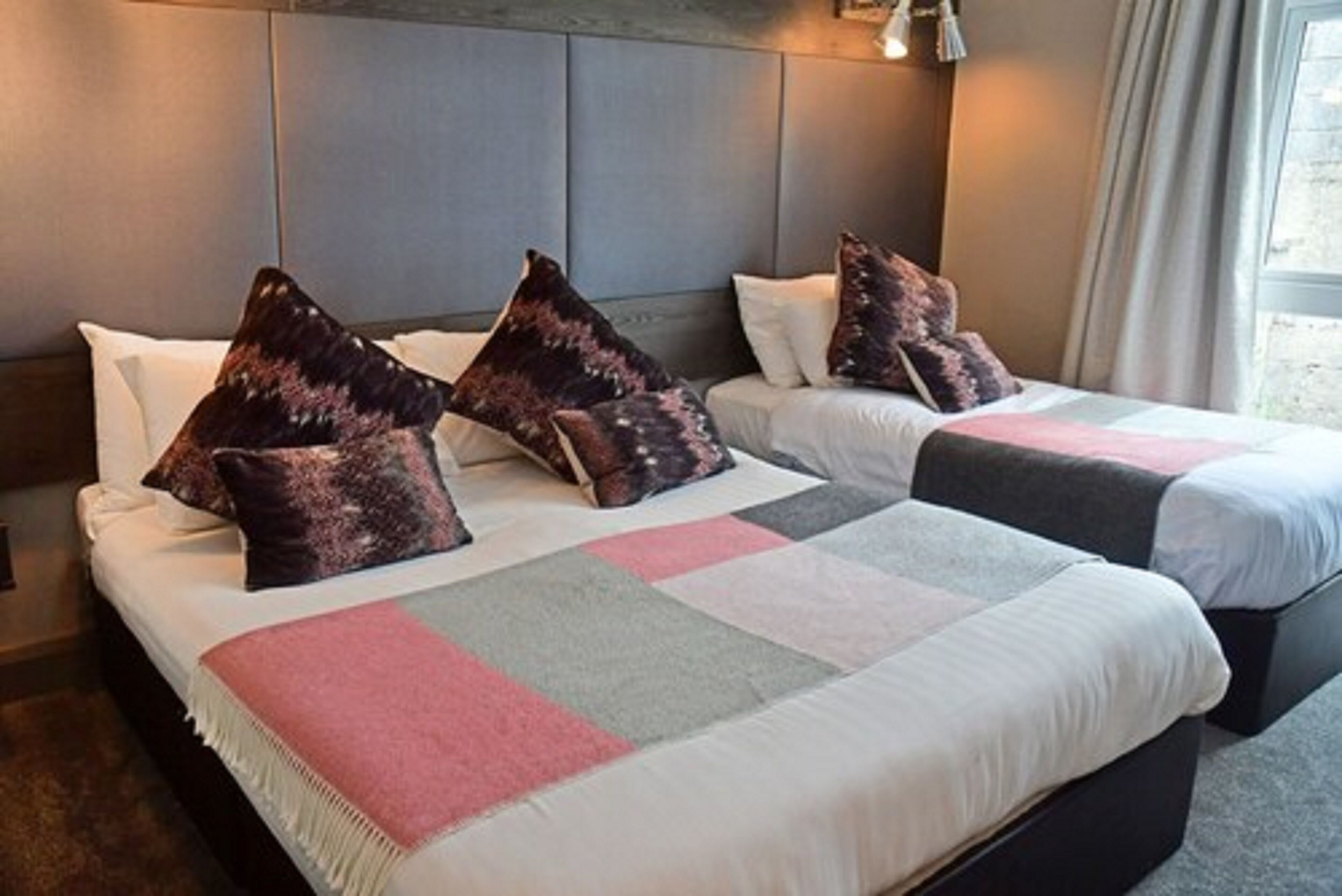 A hotel room with two beds, each with a headboard, a large window with curtains, and a neutral color scheme.