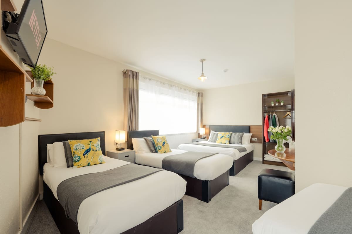 Habitación de hotel con tres camas, televisión, armario y ventana con cortinas.