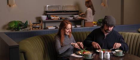 A dining area with a round table, cushioned seating, and a buffet counter in the background.