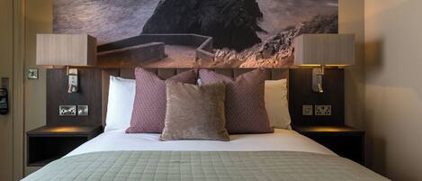 A hotel room with a bed, two bedside lamps, a nightstand, a wall-mounted telephone, and a large ocean view painting.