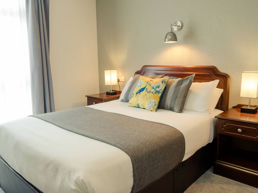 Een netjes opgemaakt bed met een grijze deken, twee kussens met een bloemenprint en twee nachtlampjes.