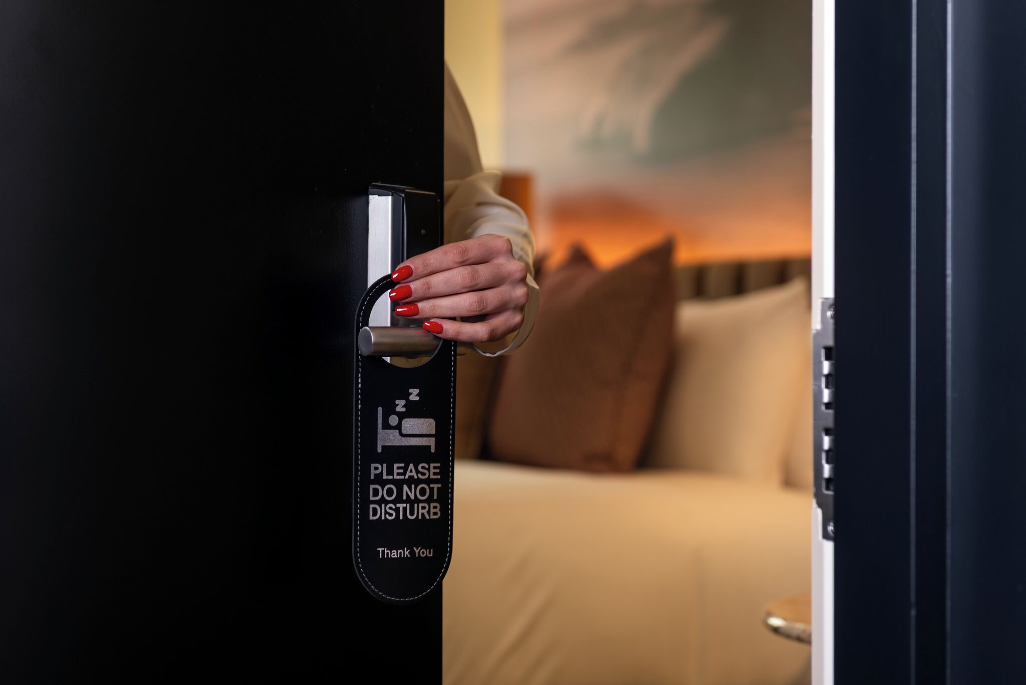 A hand opening a door with a sign that reads 'PLEASE DO NOT DISTURB.'