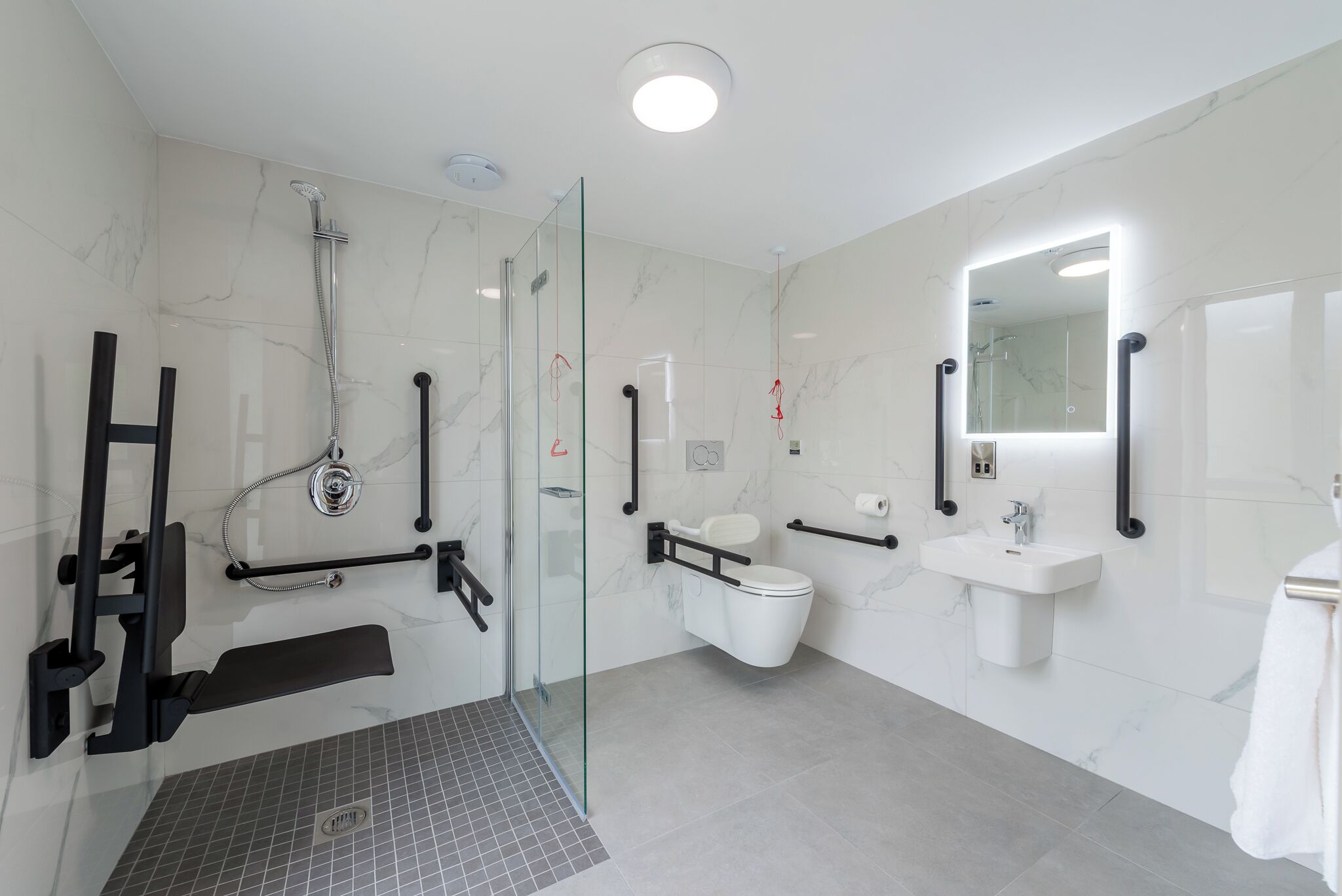Un baño moderno con cabina de ducha de vidrio, inodoro blanco, lavamanos y espejo.