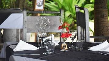 Une table dressée avec des verres à vin, un vase rempli de fleurs rouges et une chaise en bois portant une plaque avec l’inscription « SEA VIEW LODGE ».