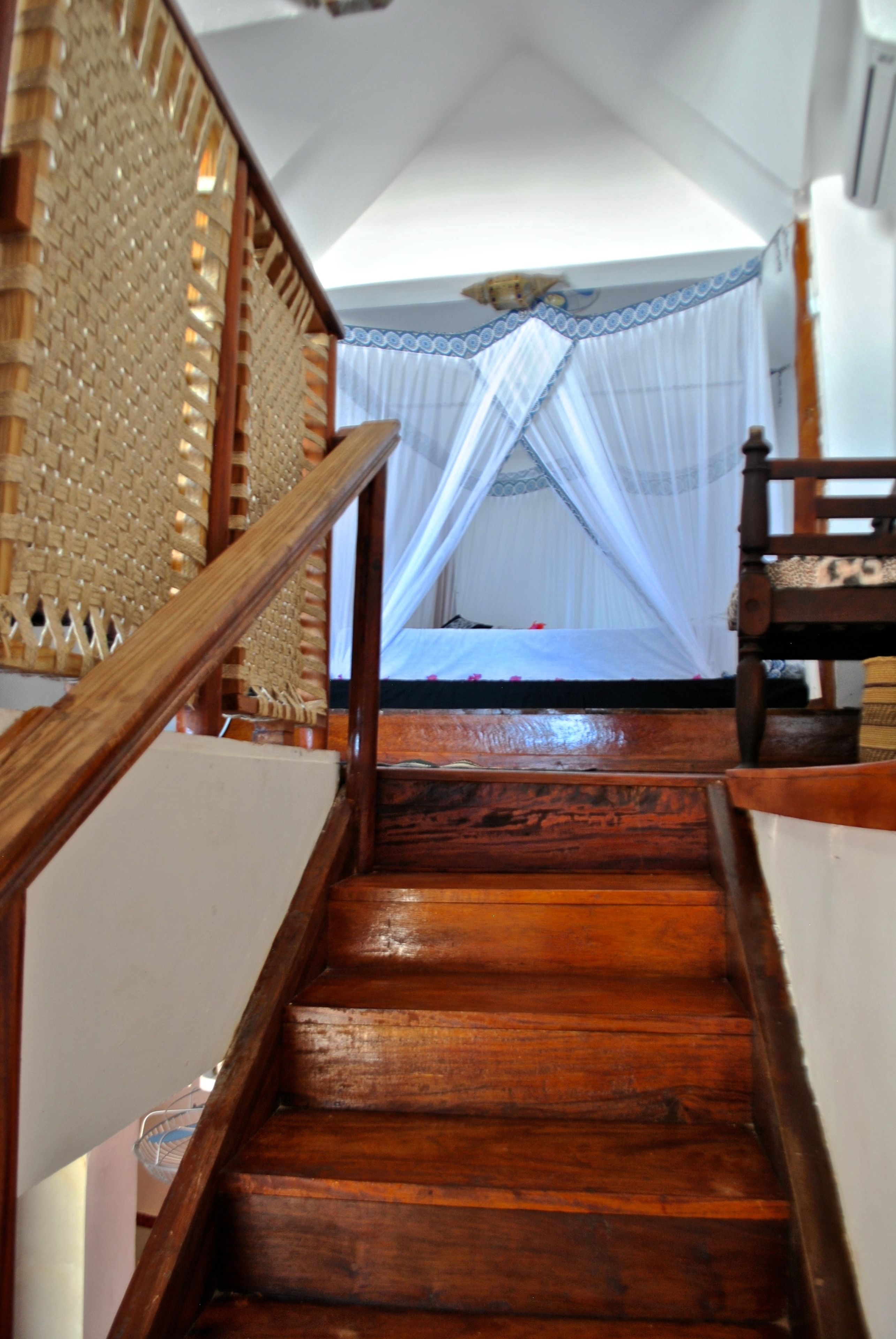 A wooden staircase leading to a room with a bed and a mosquito net.