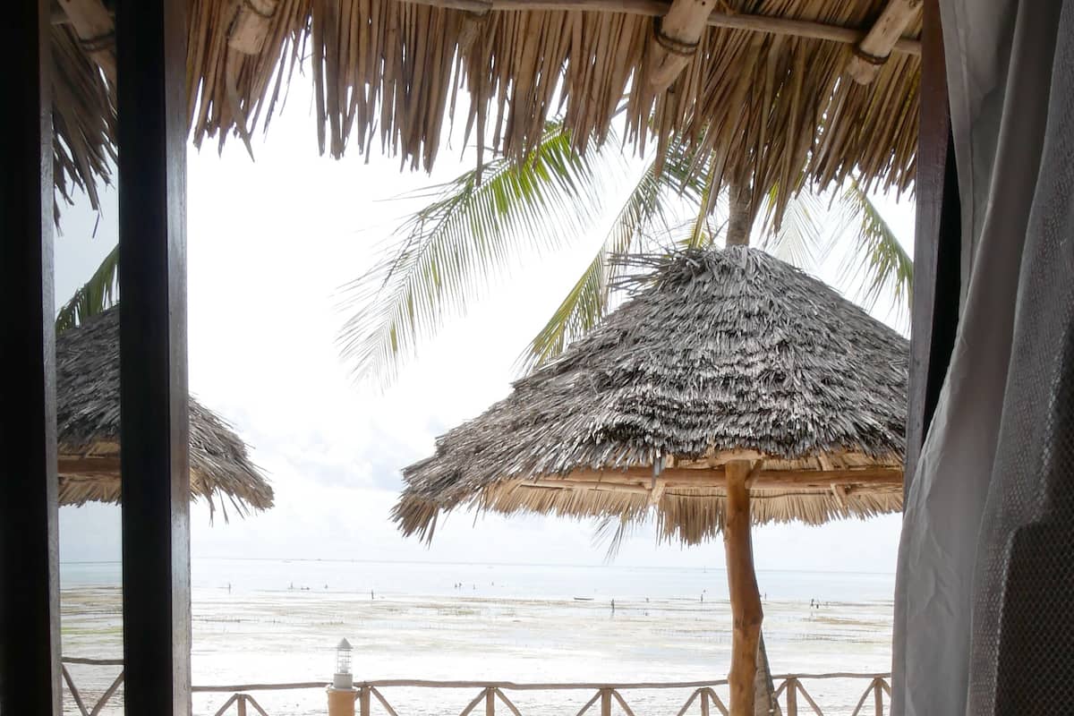 A beach view from a wooden deck with thatched umbrellas and a wooden railing.
