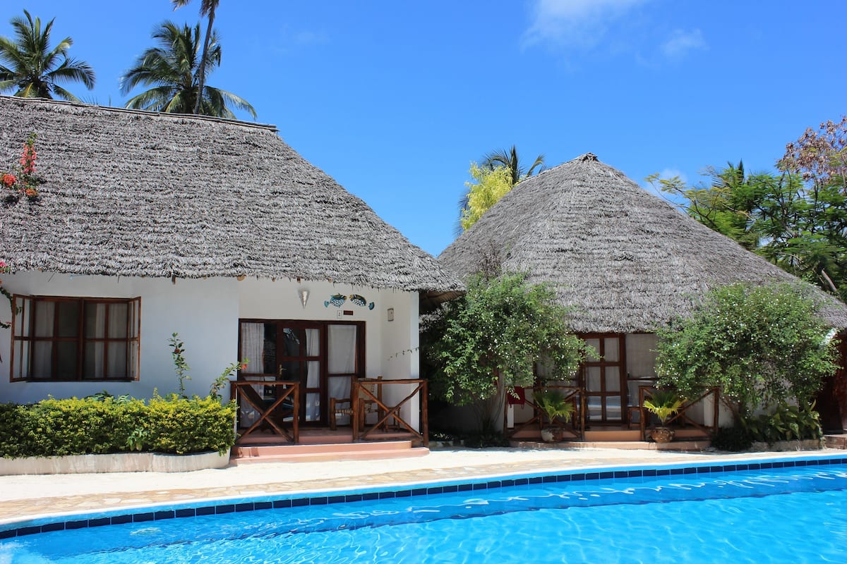 A resort with two thatched-roof cottages, a swimming pool, and tropical vegetation.