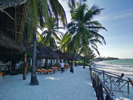 Un resort frente a la playa con cabañas de techo de paja, palmeras y sillas de descanso.