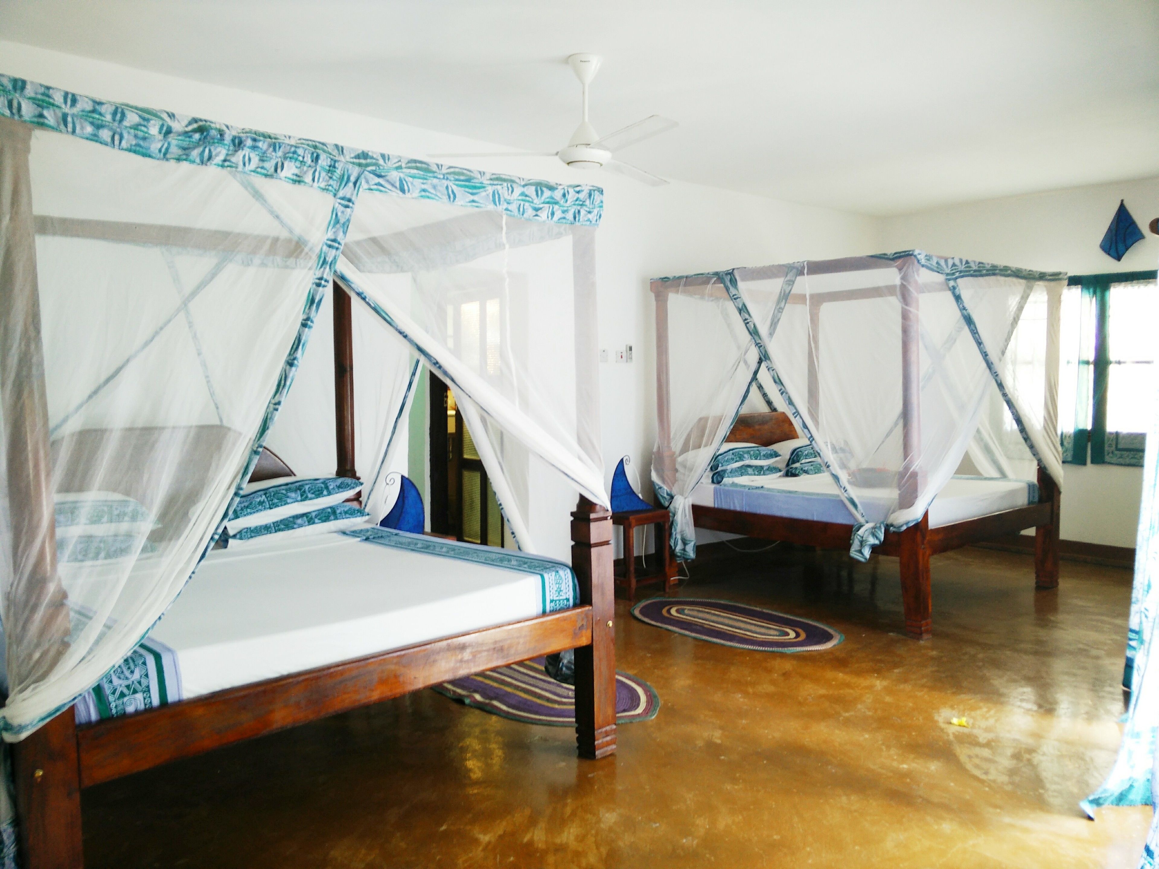 A room with two wooden beds, each with a canopy bedspread and a ceiling fan.