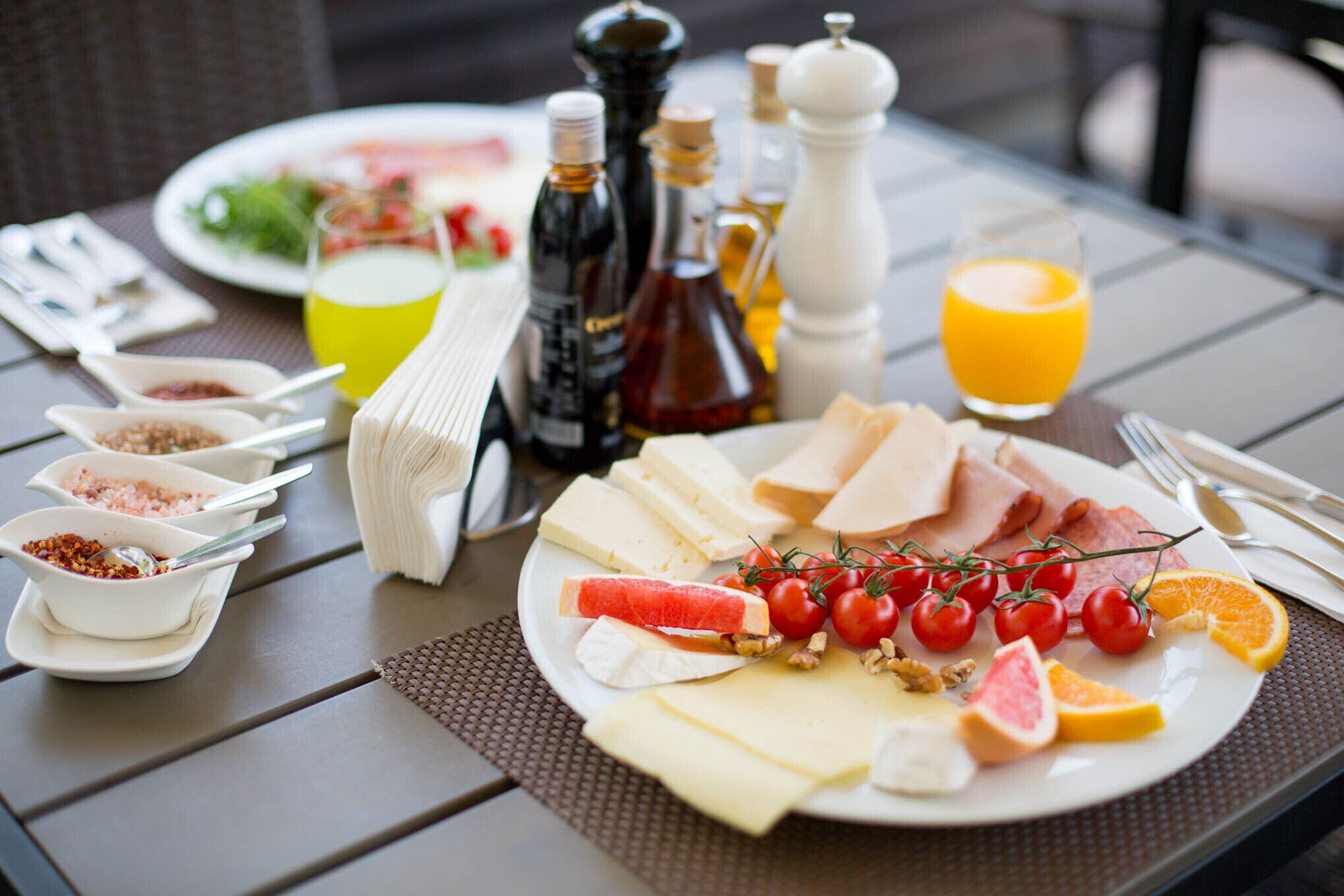 Een ontbijttafel met verschillende kazen, tomaten en een glas sinaasappelsap.
