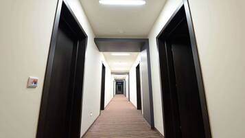 A long, narrow hotel corridor with dark doors on both sides, a patterned carpet, and a ceiling with recessed lighting.