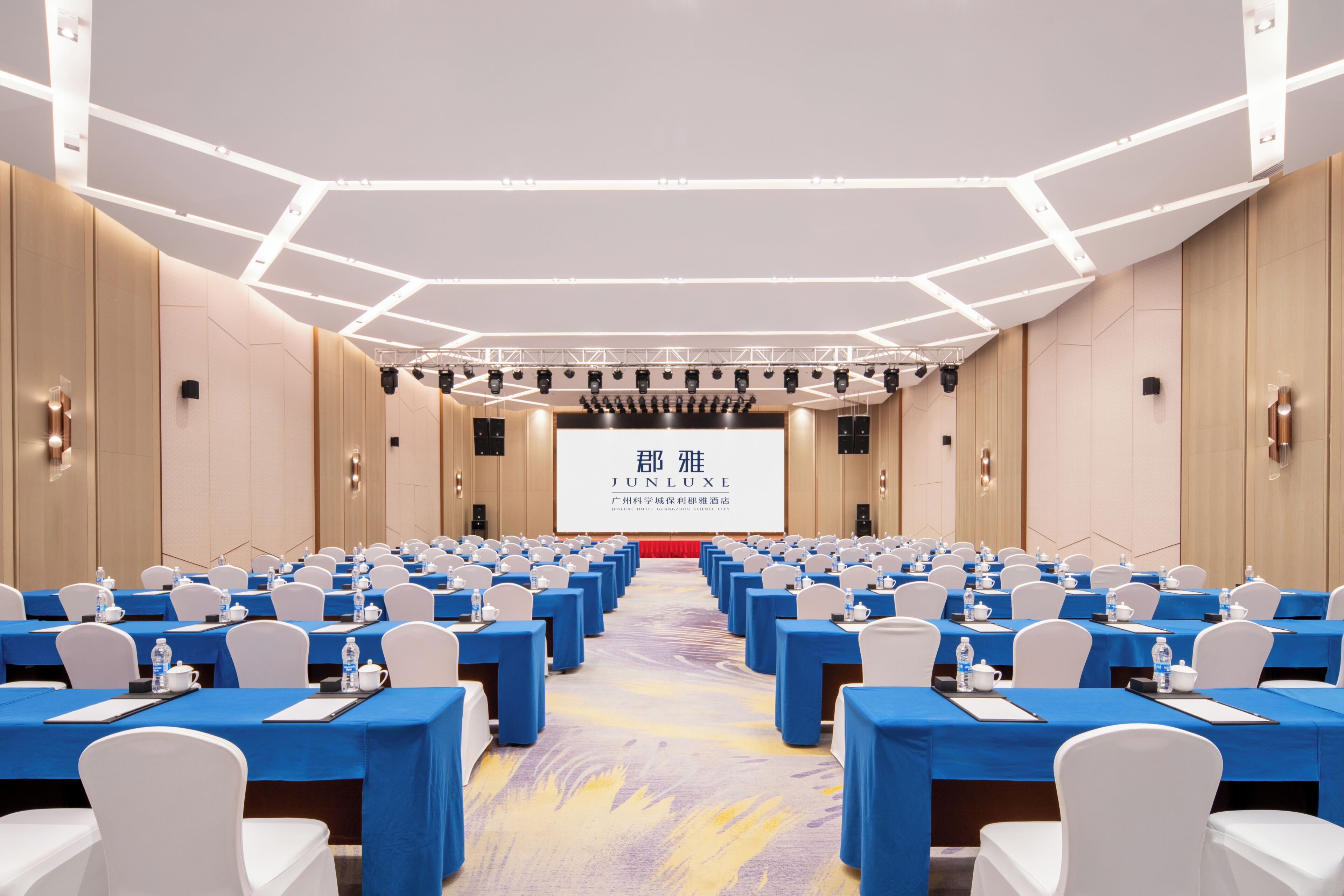 A conference room with rows of tables, chairs, and a large screen at the front.