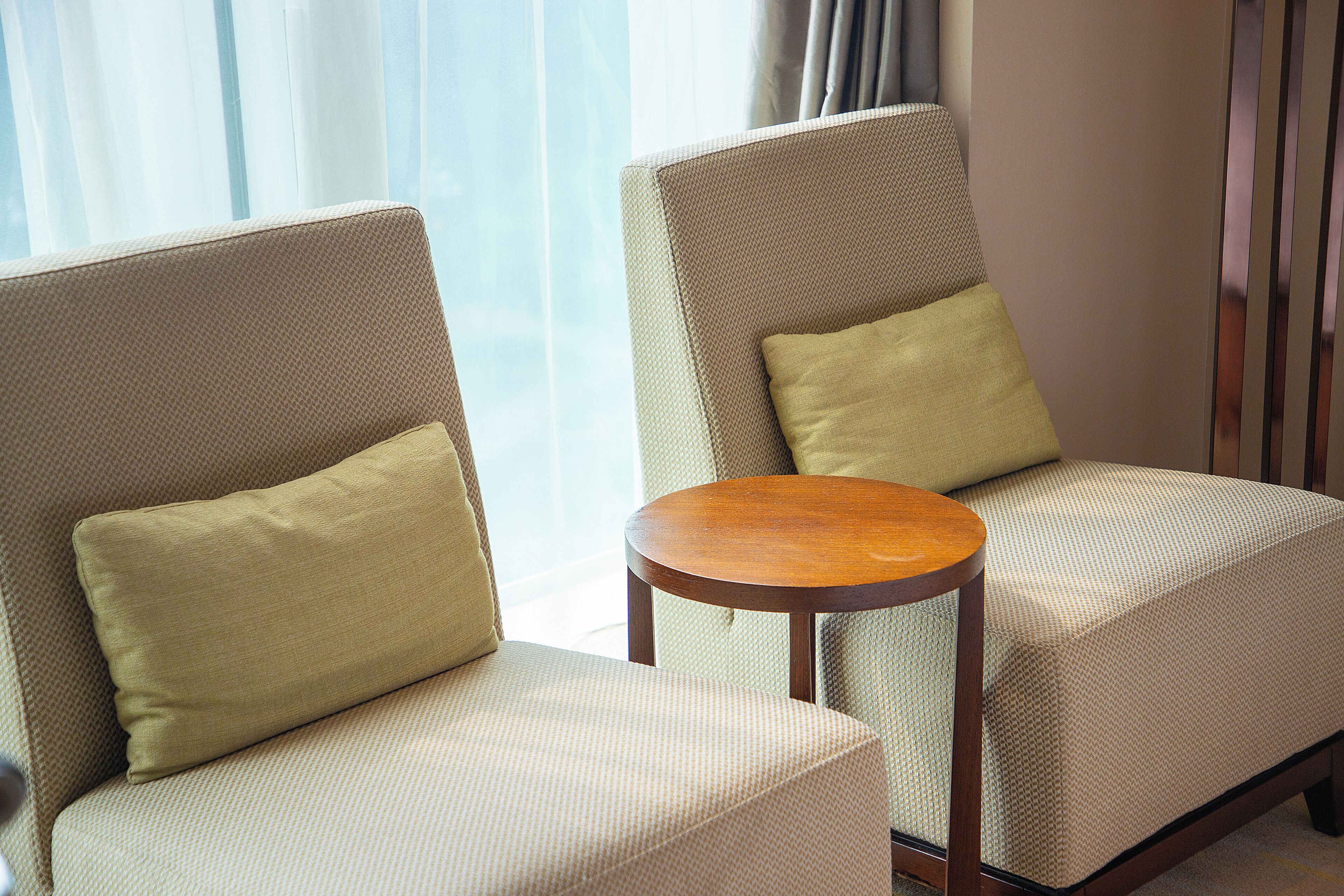 Two armchairs with cushions, a small wooden table, and a view of a window with curtains.